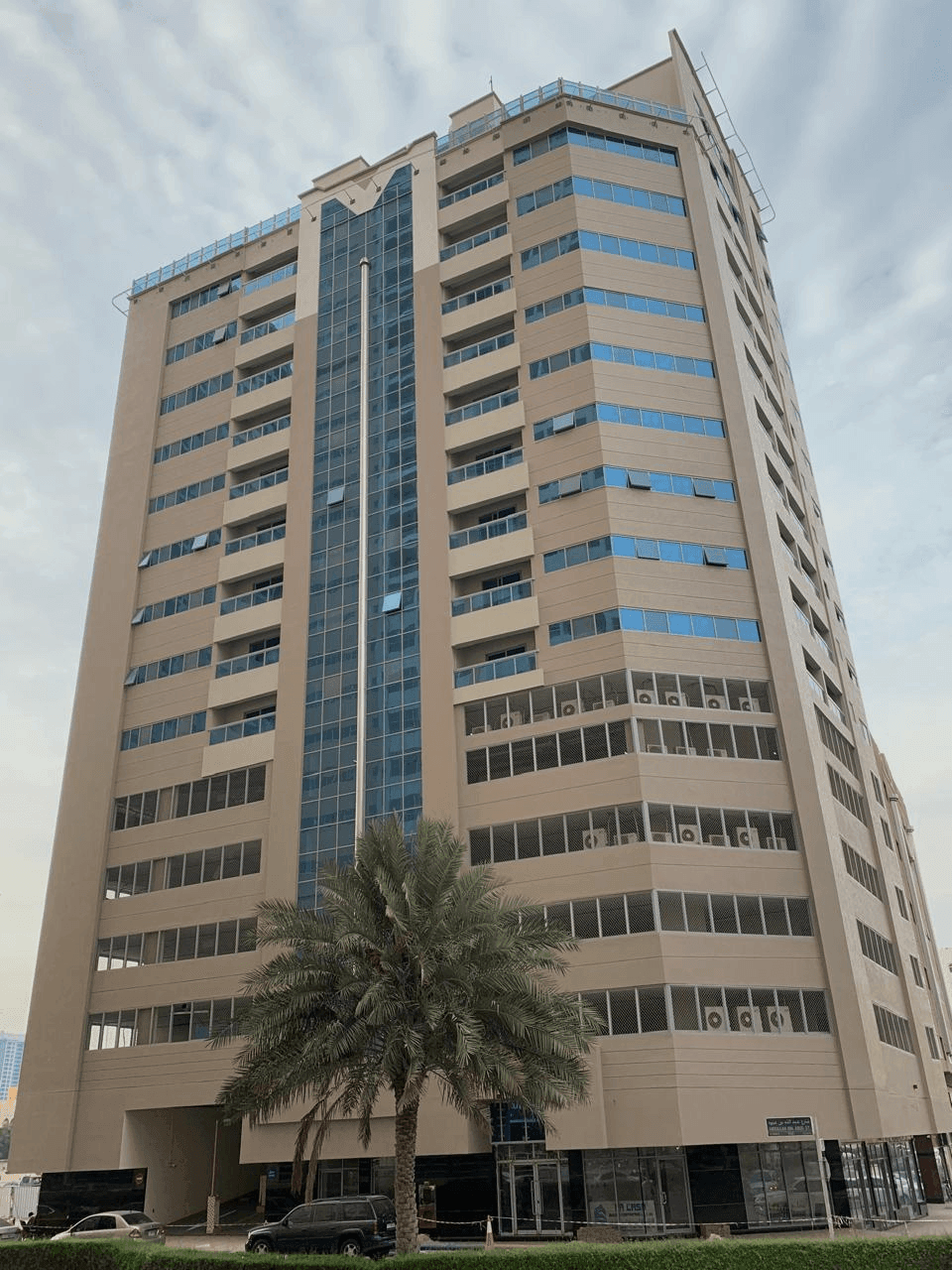 Tall beige building with multiple windows, blue glass accents, and a palm tree in front.